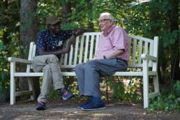 Diverse care giver, nurse sitting on park bench with elderly man