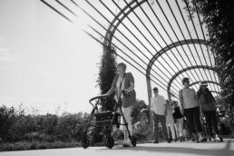 senior woman using a walker on a walking path at a park with a group of friends