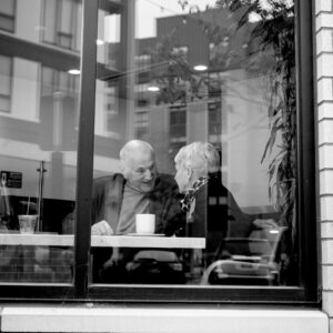 Senior man and woman having coffee at table seen through window